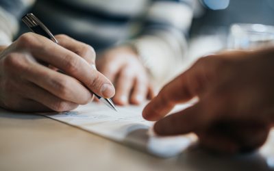 Close up of unrecognizable man signing a contract while financial advisor is aiming at the place he need to sign.