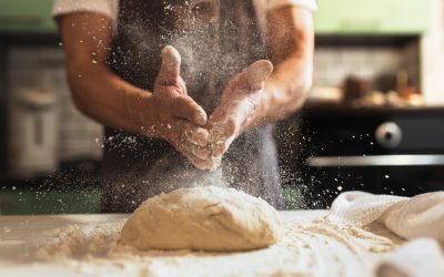 Kneading dough. Male chef in kitchen chef's apron spraying flour over dough