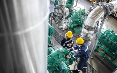 Gas and oil industrial workers working together and checking pipeline and engine pumps in factory.