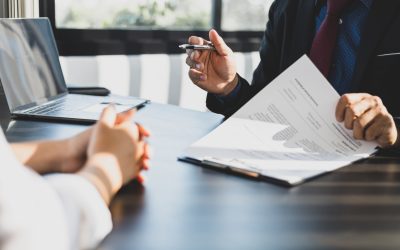 Businessman in suit in his office showing an insurance policy and pointing with a pen where the policyholder must to sign. Insurance agent presentation and consulting insurance detail to customer.