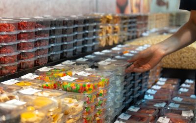 Customer choosing colorful candied fruit in a well-stocked grocery store filled with sweets and treats, shelves lined with packaged goodies bursting with vibrant colors and flavors