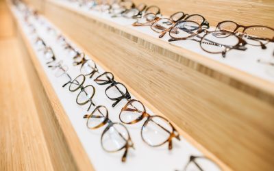 Assorted styles of eyeglass frames for sale line a display case in a retail store.