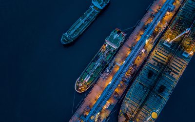 Aerial view Crude oil tanker under cargo operations on typical shore station with clearly visible mechanical loading arms and pipeline infrastructure.